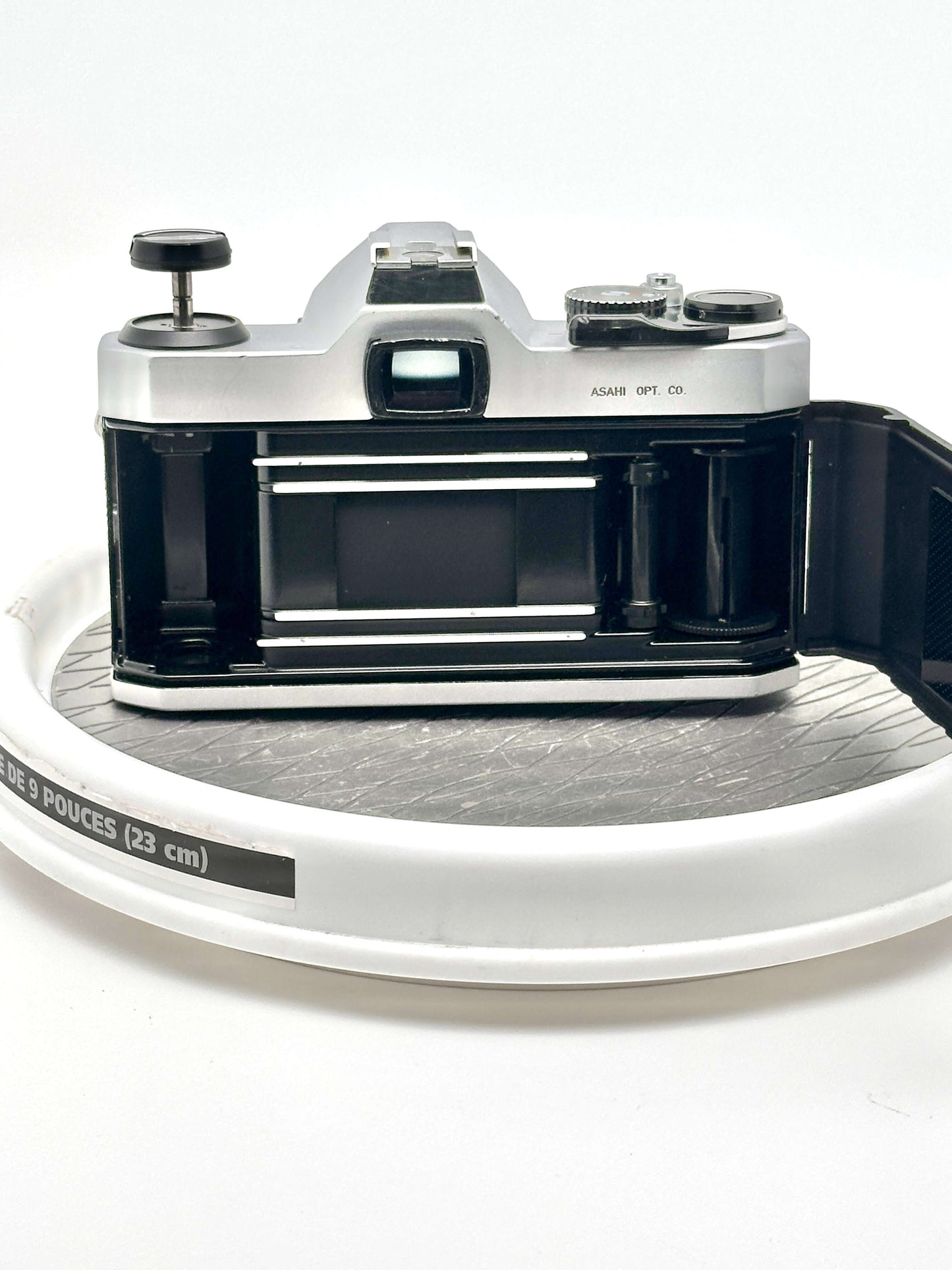 Pentax K1000 black 35mm film camera rear view on a white display turntable.