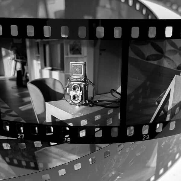 Black and white film reel with a vintage camera on a table in a bright interior setting.