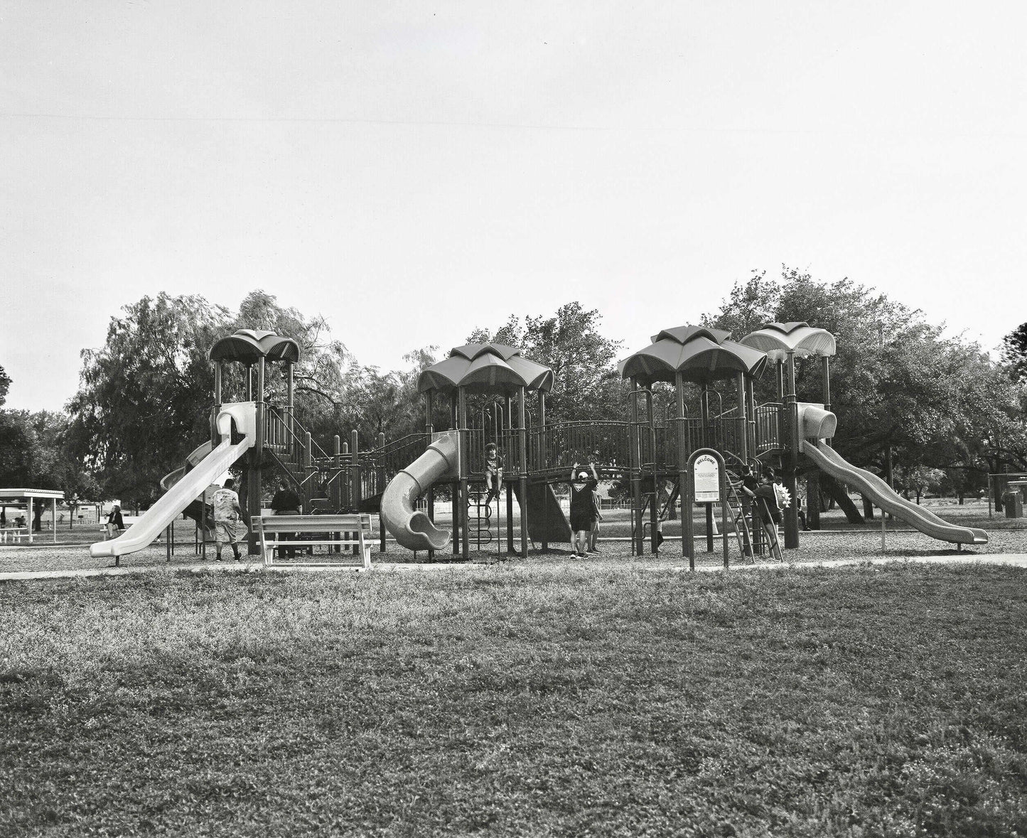 Black and white photo of a playground with slides and children playing in a park.