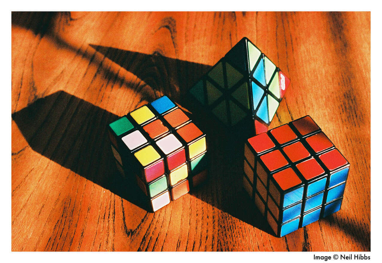 Colorful Rubik's cubes in various designs arranged on a wooden surface with dramatic shadows.