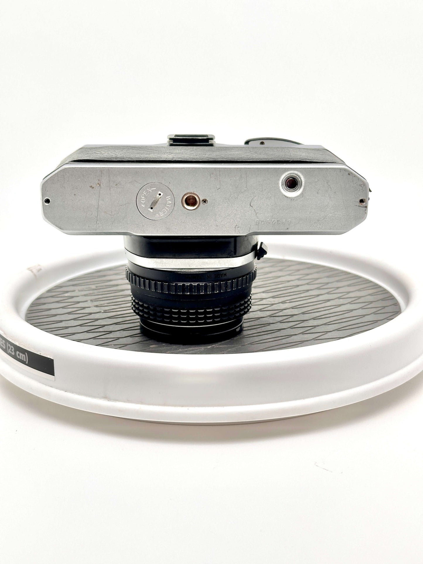 Top view of Japanese Asahi Pentax K1000 black 35mm film camera with 50mm f2 lens on white display stand.