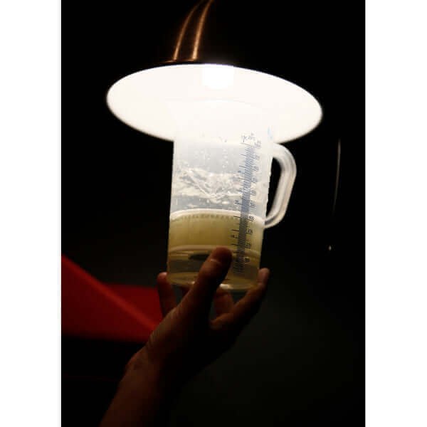 Hand holding a measuring cup under a lamp, showcasing liquid for black and white slide processing.