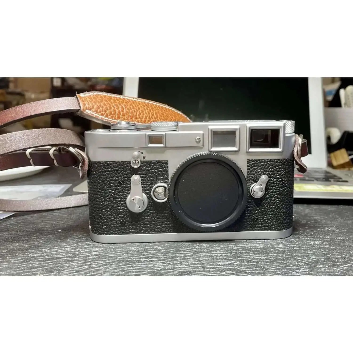 Silver and black leather-bodied leica m3 rangefinder camera with a tan leather strap.