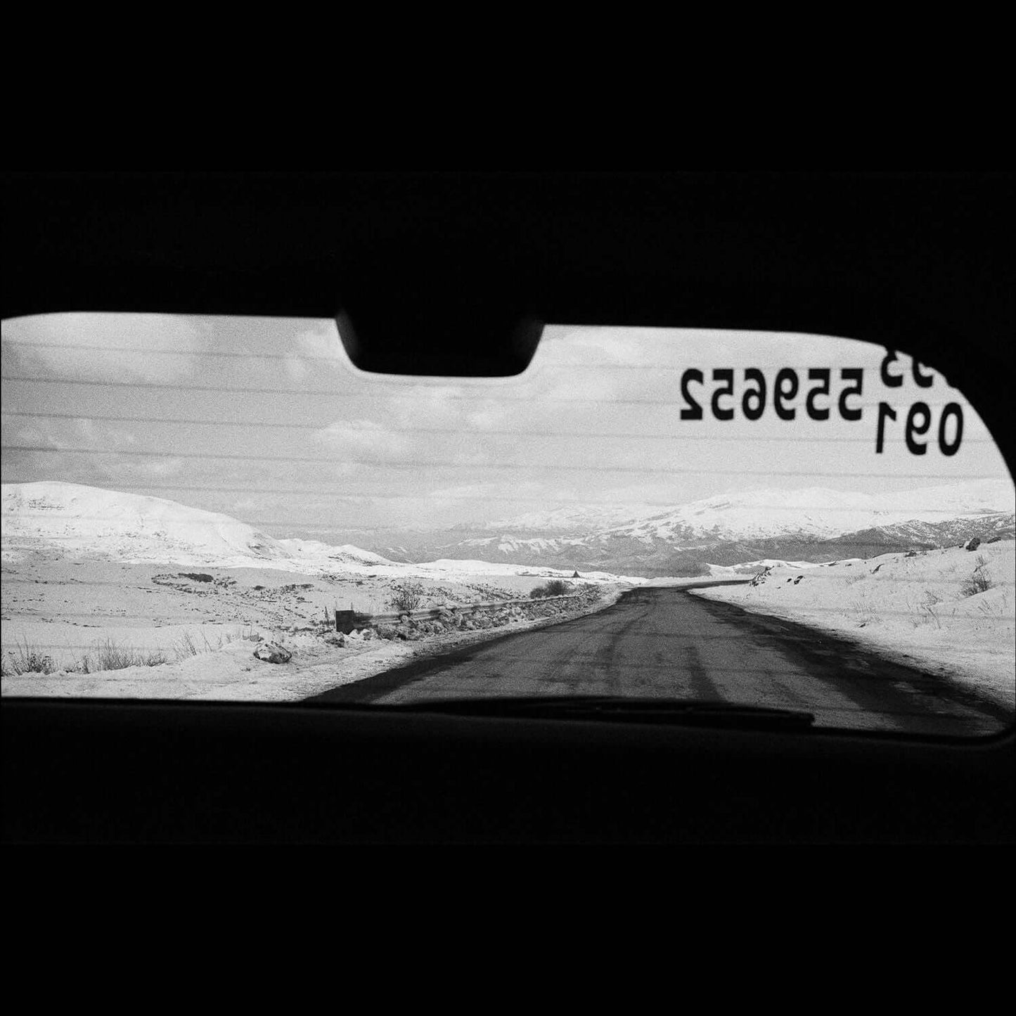 View through car rear window of a snowy road in black and white, captured on Bergger Pancro 400 ISO film.