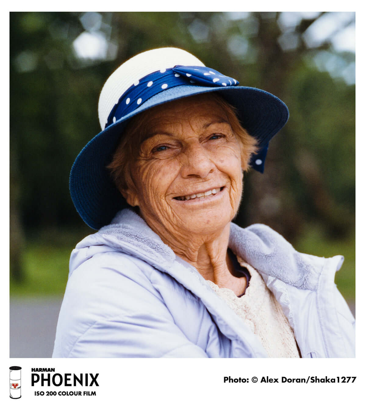 Elderly woman smiling outdoors wearing a hat, captured on HARMAN Phoenix 200 ISO color film for an analog adventure experience.