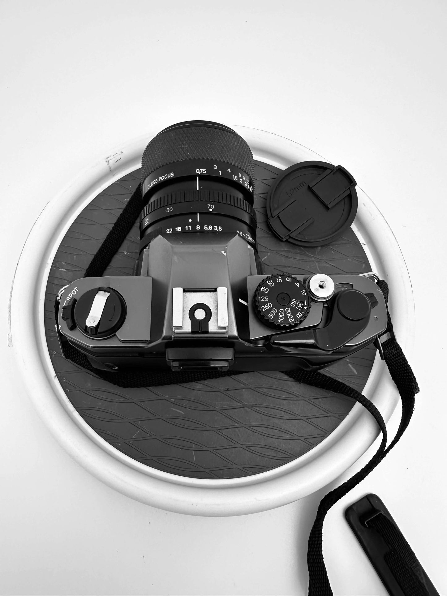 Top view of Olympus OM 2000 film camera with 35-70mm f/3.5-4.8 lens, showing controls, strap, and lens cap in black and white.