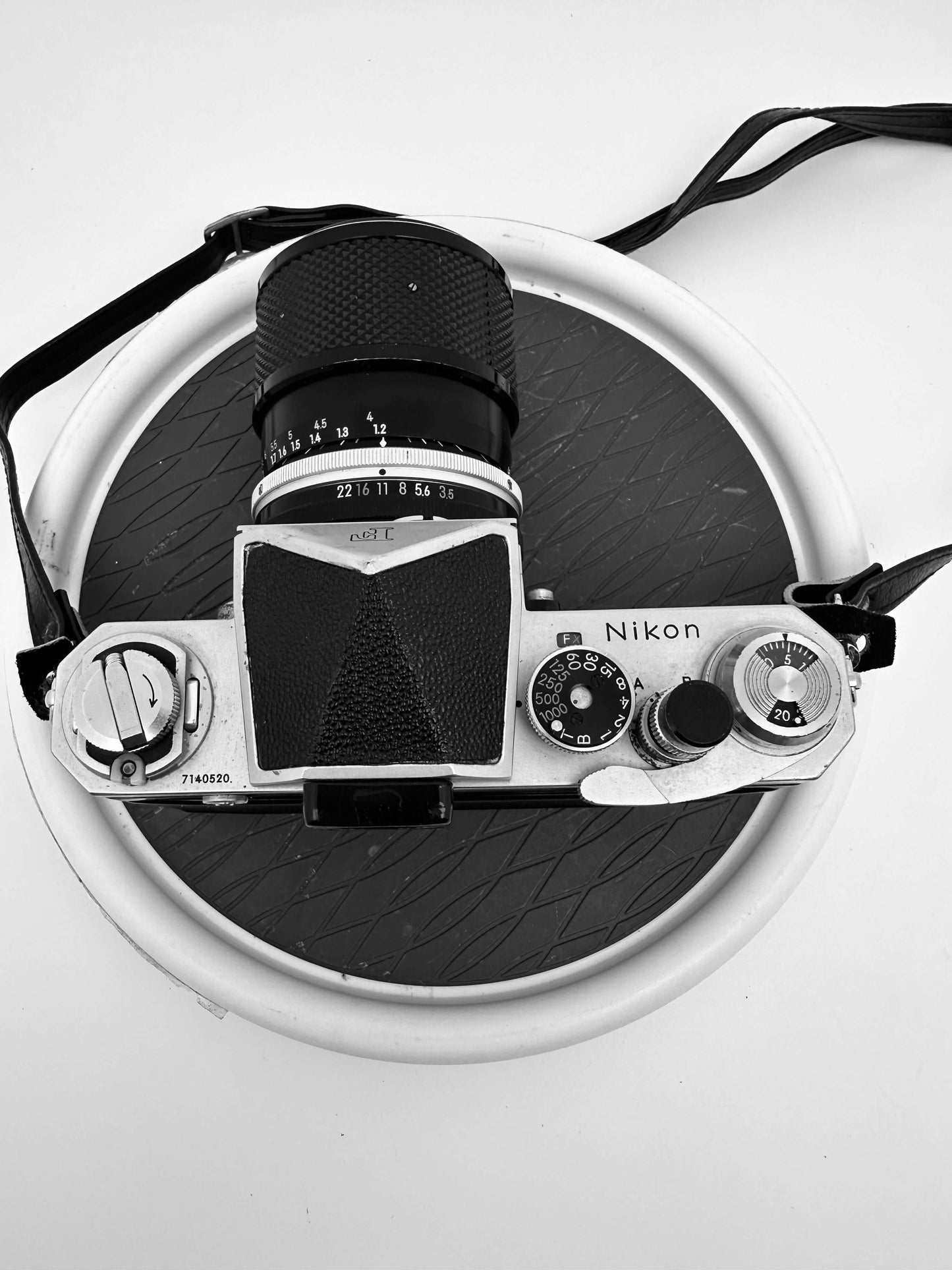 Vintage Nikon F 35mm film camera with Nikkor 43-86mm f/3.5 zoom lens, showing wear and tear, top view against circular background.