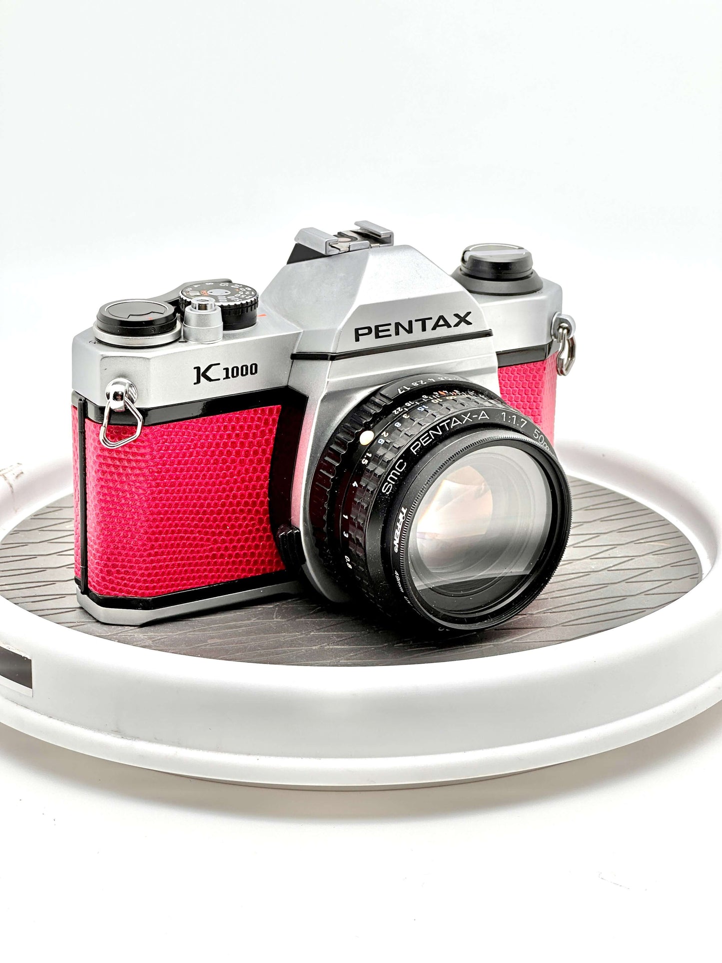 Japanese Asahi Pentax K1000 Red 35mm film camera with 50mm f1.7 lens on a rotating display.