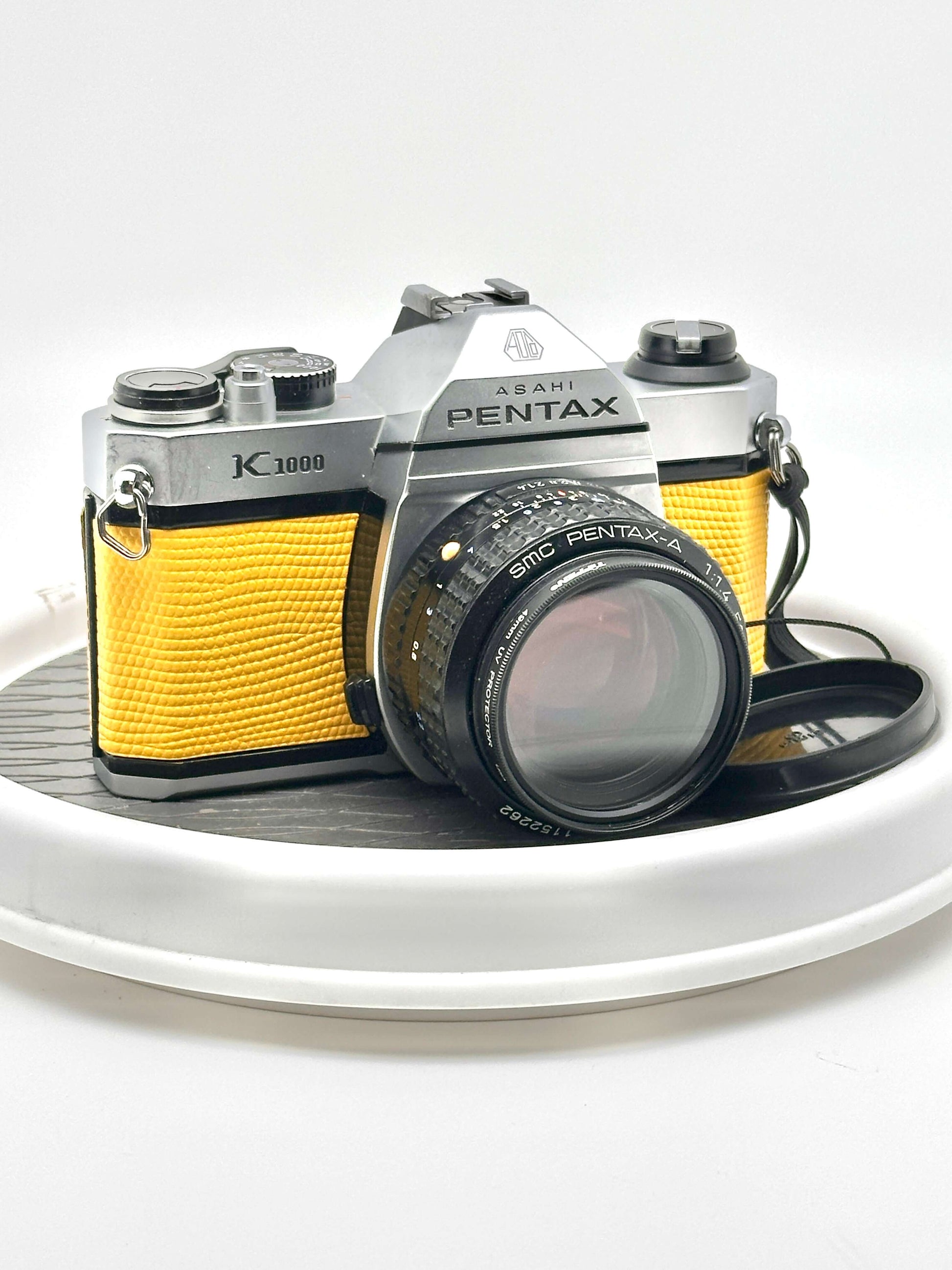 Japanese Asahi Pentax K1000 used 35mm film camera in yellow with 50mm f1.4 lens on display.