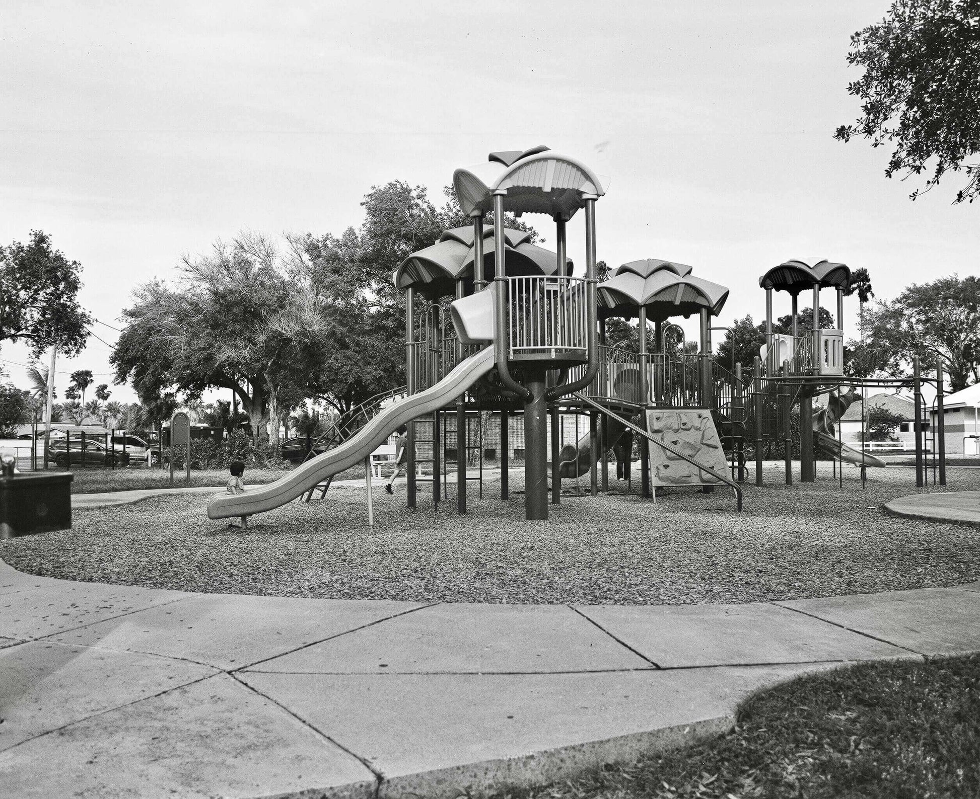 Outdoor playground with various climbing structures, slides, and swings in a park surrounded by trees.