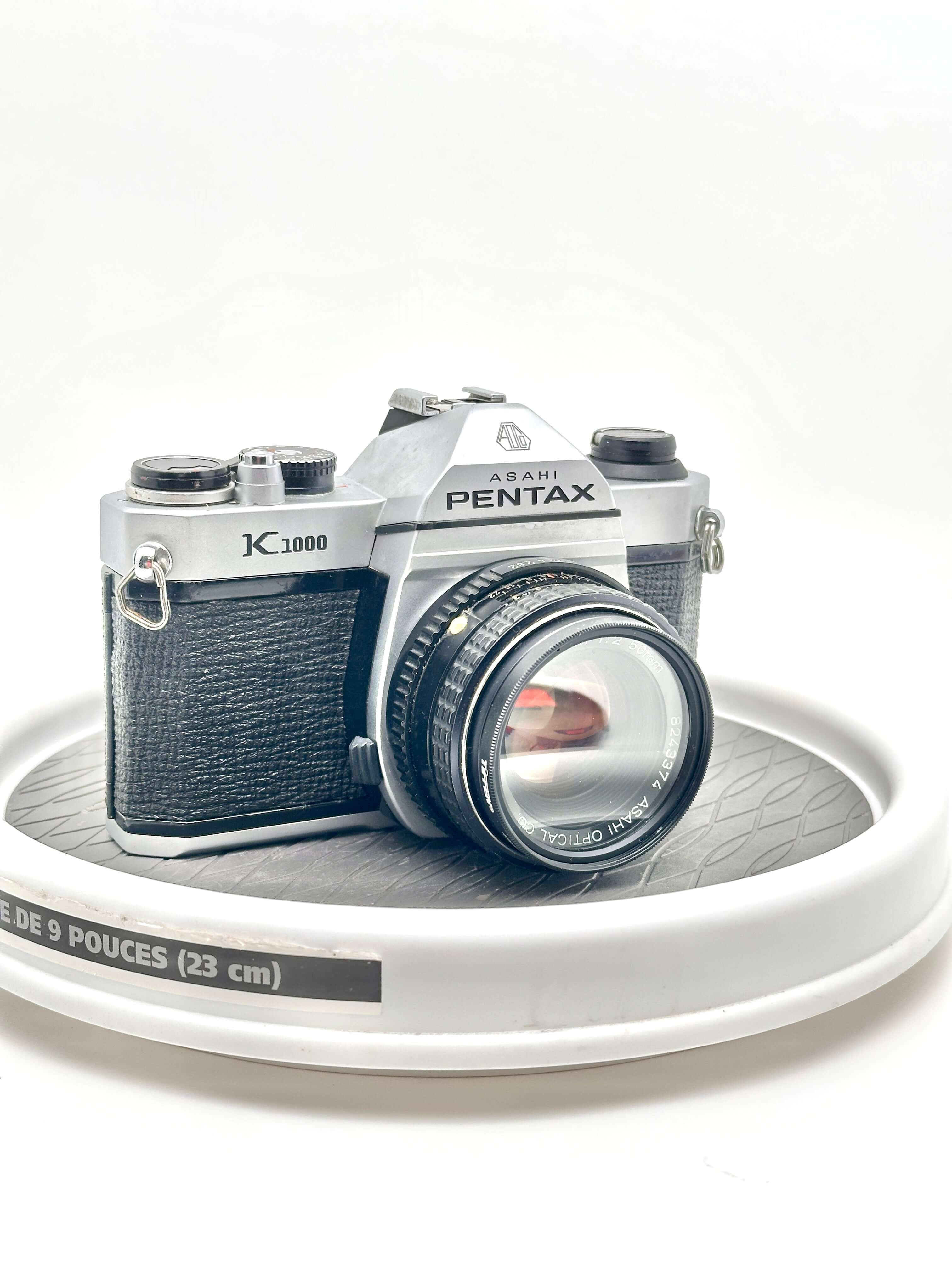 Asahi Pentax K1000 black 35mm film camera with 50mm f2 lens displayed on a rotating stand.