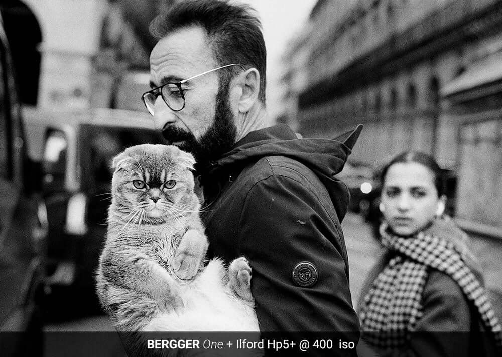 Man holding a cat in his arms, street view in the background, BERGGER ONE + Ilford Hp5+ @ 400 ISO film example.