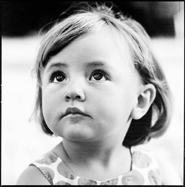 Black and white portrait of a young child gazing upwards with a thoughtful expression.