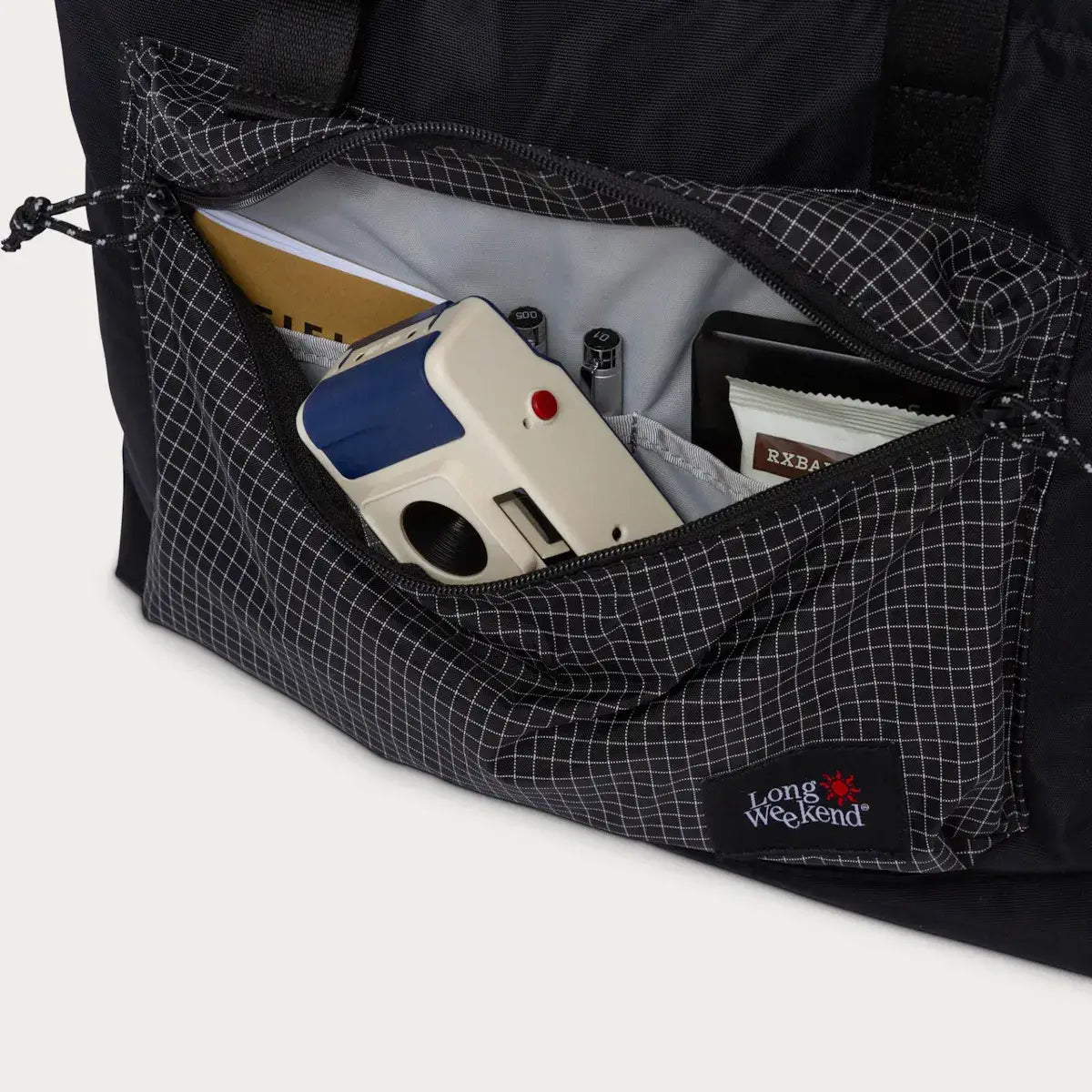 Front pocket of Long Weekend bag with a camera, notebooks, pens, and a wallet, highlighting organized storage and convenience.