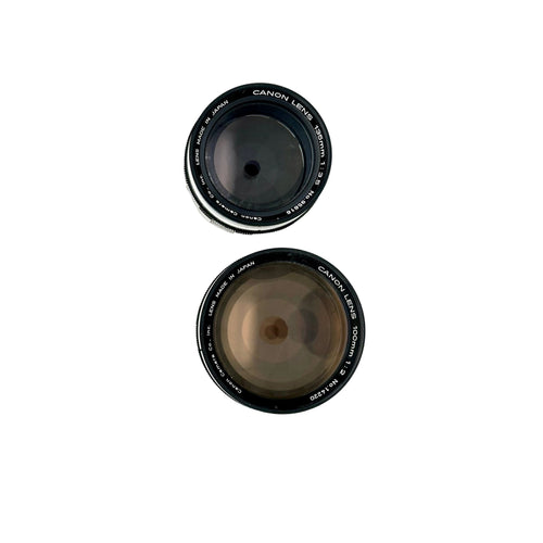 Two black canon camera lenses, one 50mm f/1.4 and the other 100mm f/2, with silver lettering on their rings.