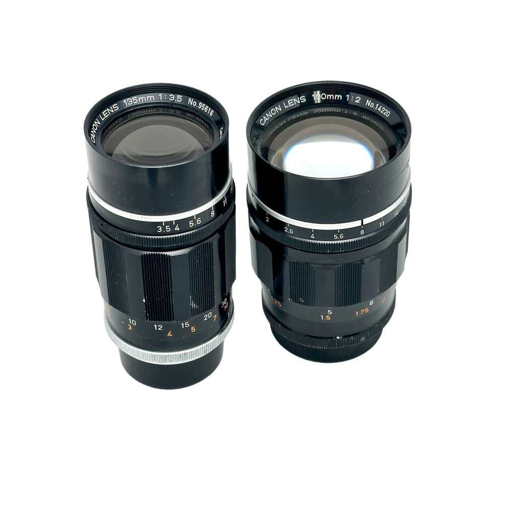 Two black canon camera lenses with silver metallic rings and engraved markings, one labeled 195mm f/3.5 and the other 100mm f/2.