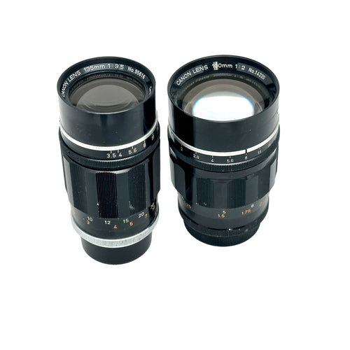 Two black canon camera lenses with silver metallic rings and engraved markings, one labeled 195mm f/3.5 and the other 100mm f/2.