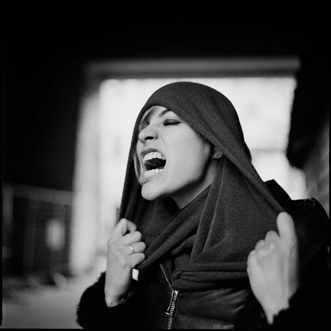 Black and white portrait of a woman expressing emotion, wearing a scarf in an urban setting.