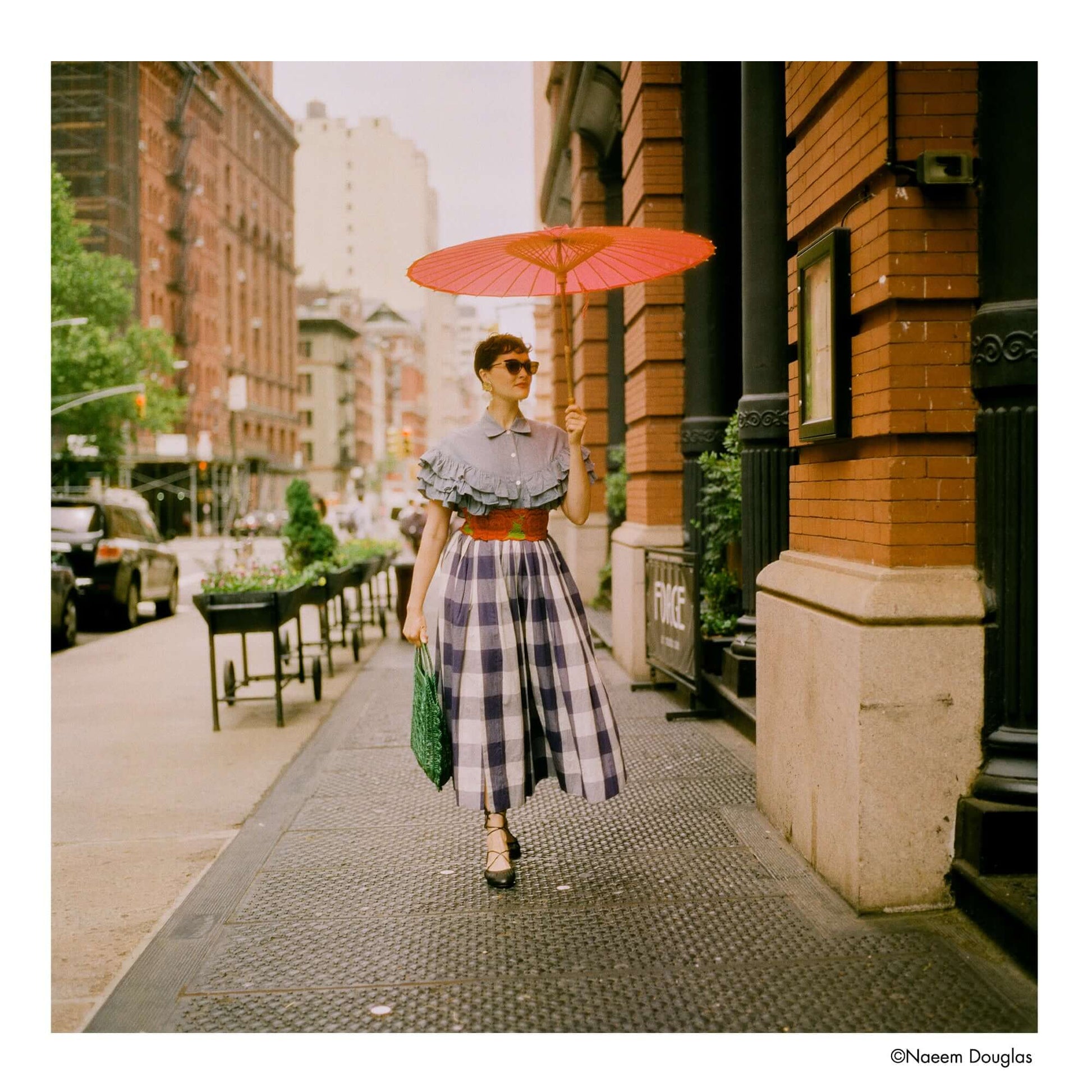 Woman in stylish outfit with red parasol walking in urban street, captured on Harman Phoenix II 200 ISO Color 120 Medium Format Film.