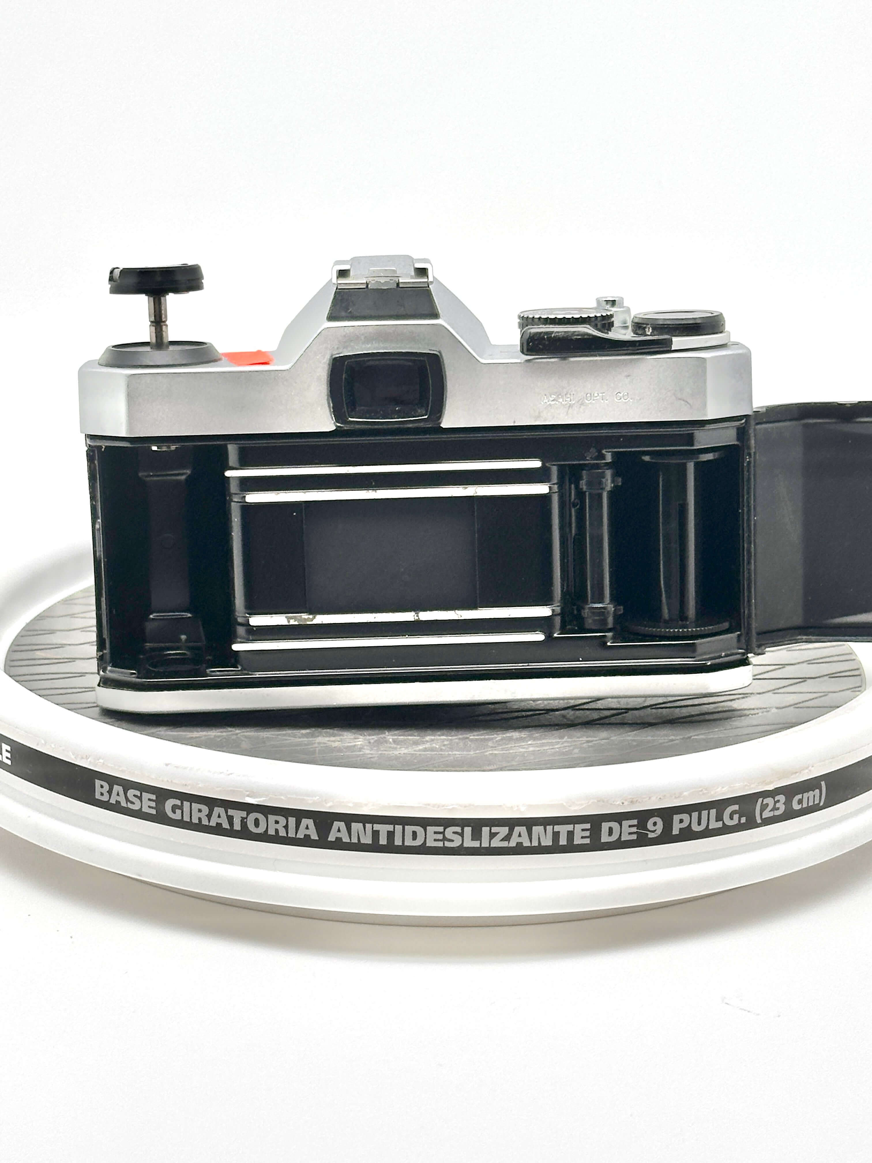 Pentax K1000 black 35mm film camera rear view on a round surface, showcasing its empty film compartment.