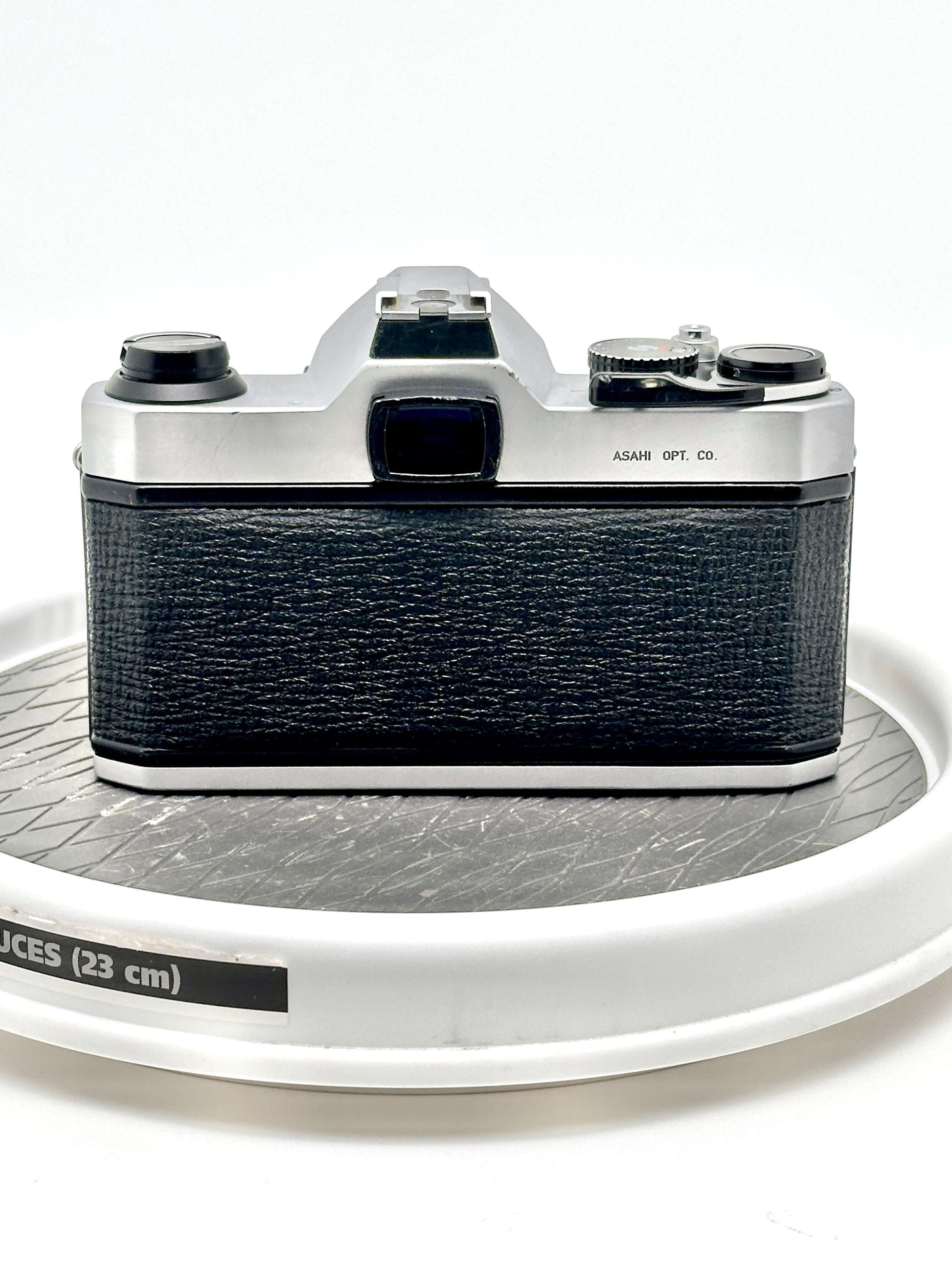 Pentax K1000 black 35mm film camera back view on a round display, showcasing robust design and vintage aesthetic.