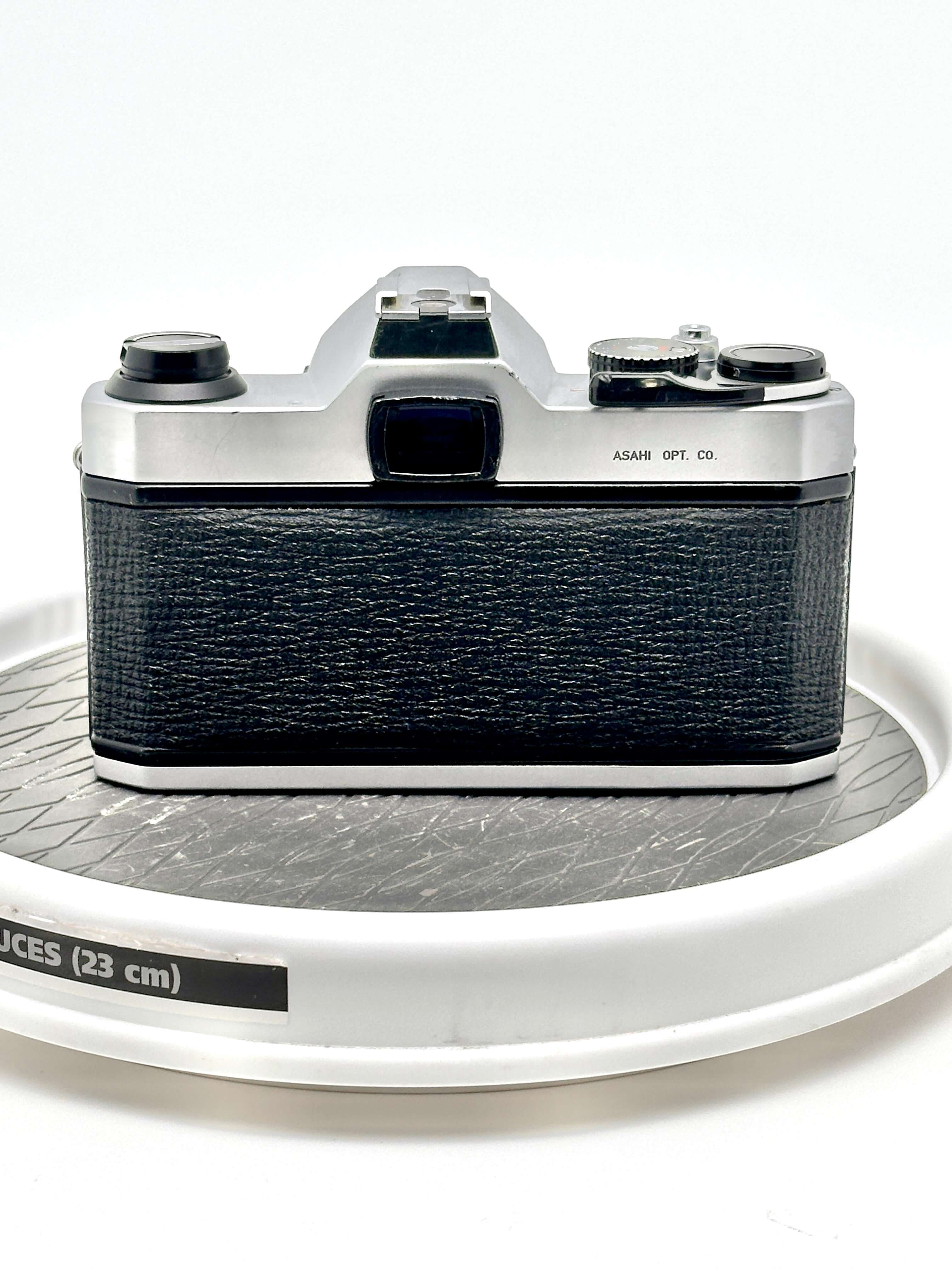 Pentax K1000 black 35mm film camera back view on a round display, showcasing robust design and vintage aesthetic.