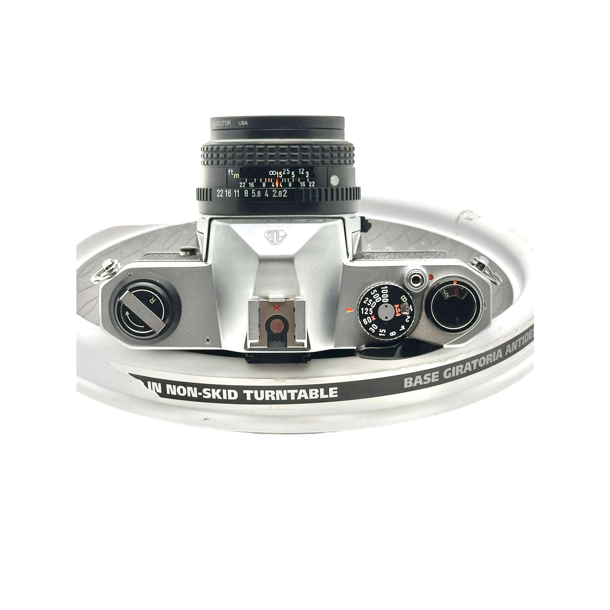 Silver-bodied canon ae-1 film camera with a black lens mounted on top, resting on a white turntable.