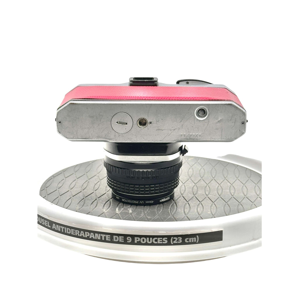 A vintage silver-bodied camera with a vibrant pink textured top panel and a black lens mounted on it.