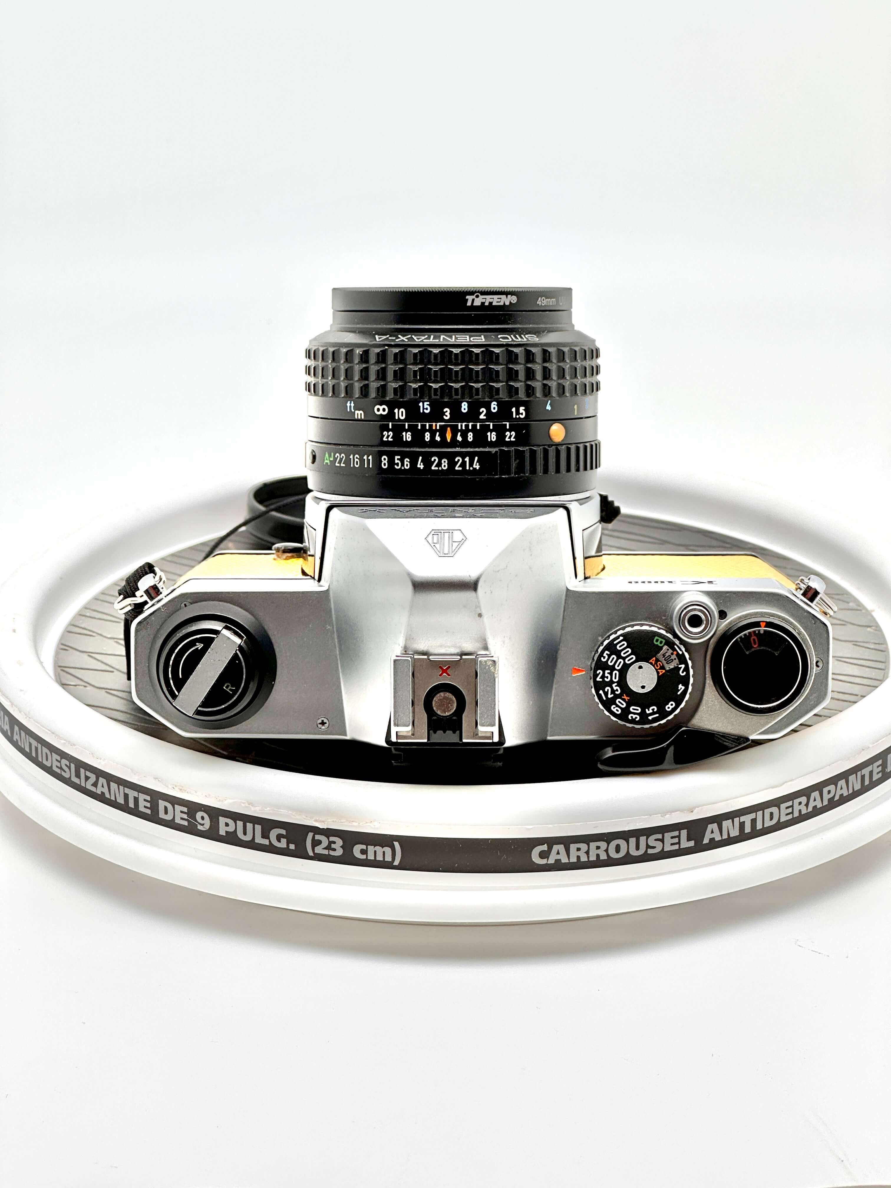 Japanese Asahi Pentax K1000 yellow 35mm film camera on a rotating display, featuring 50mm f1.4 lens.