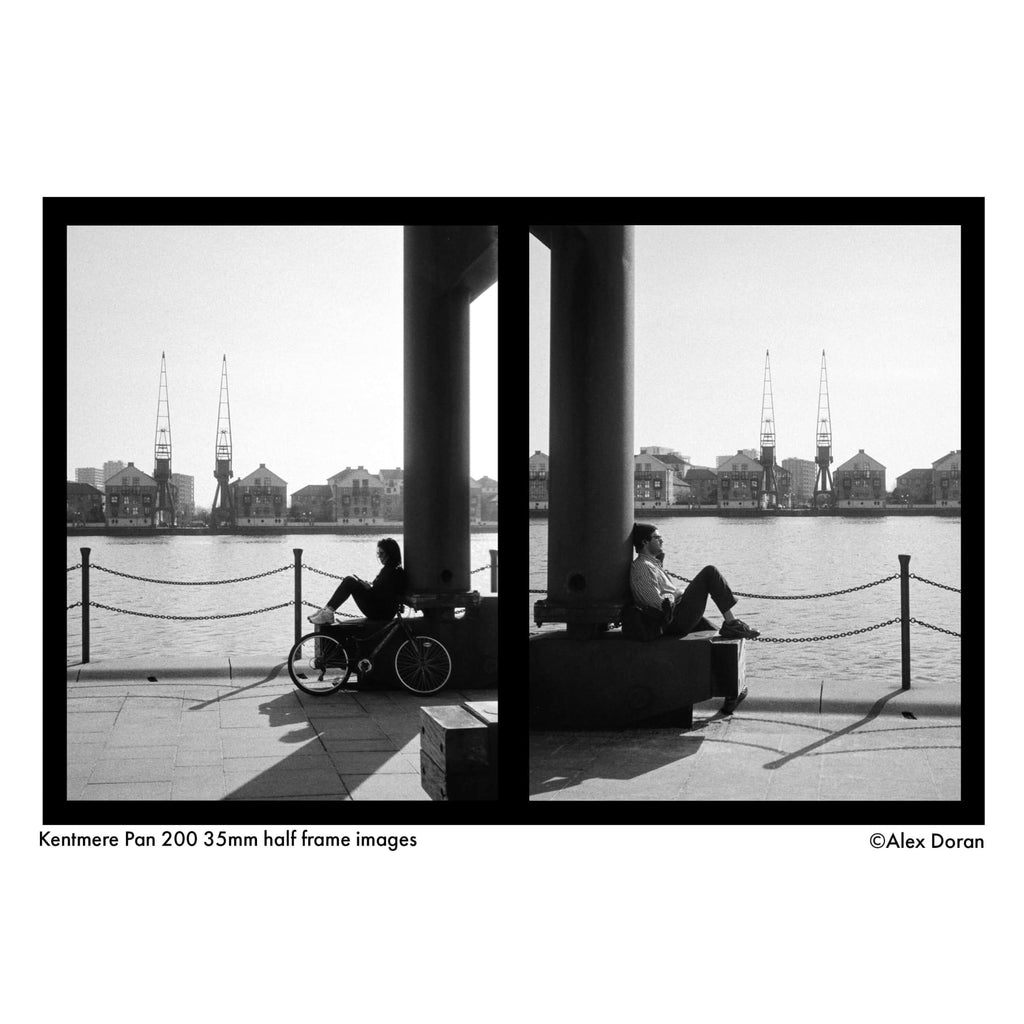 The image is a black and white diptych photograph featuring two individuals seated on stone benches beside a waterfront, with industrial cranes visible in the background.