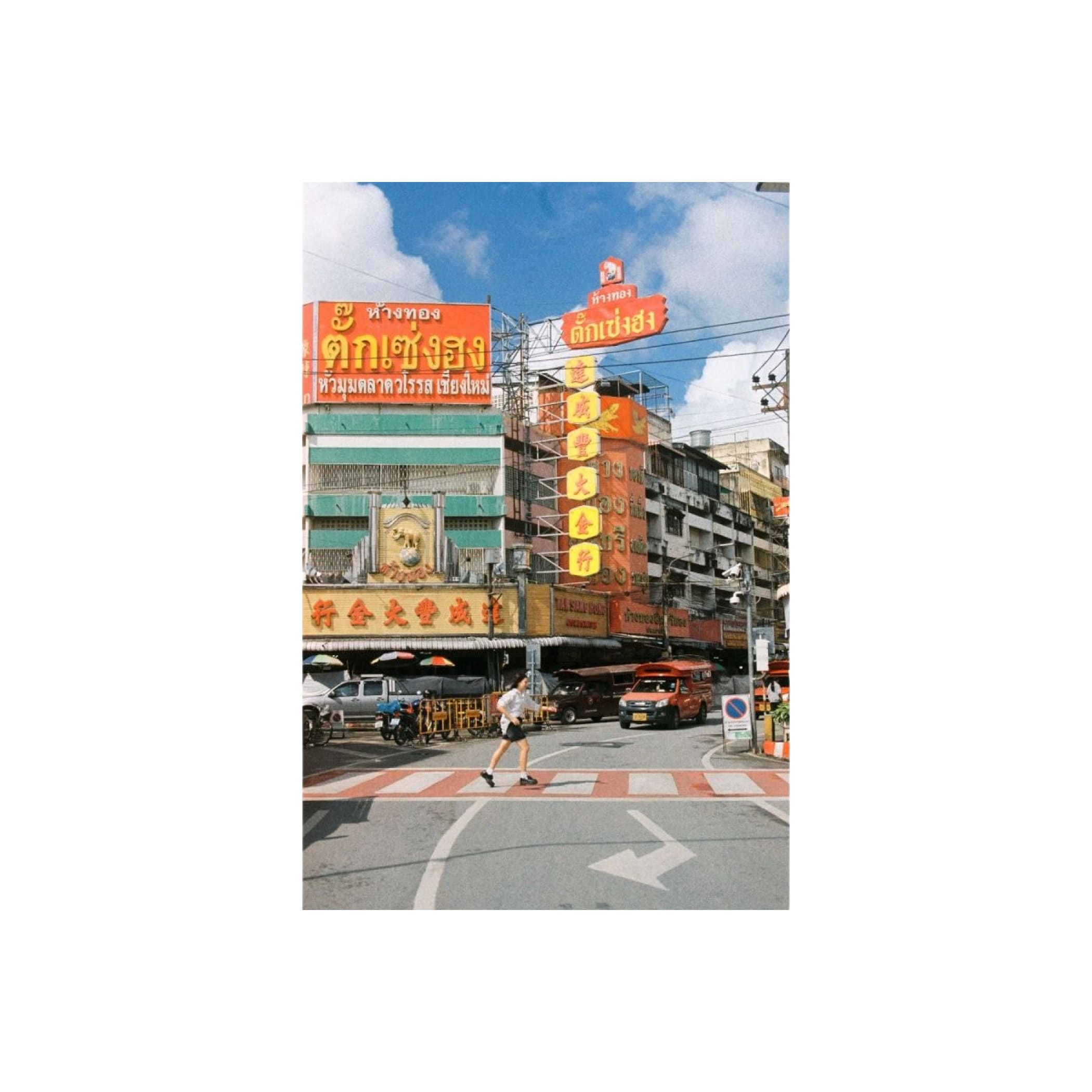 The image features a vibrant orange neon sign with thai script, mounted on the side of a multi-story building in an urban setting.