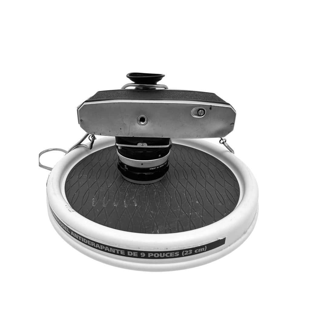 Vintage silver-bodied camera with a textured black top and lens mounted on an anti-slip circular stand.
