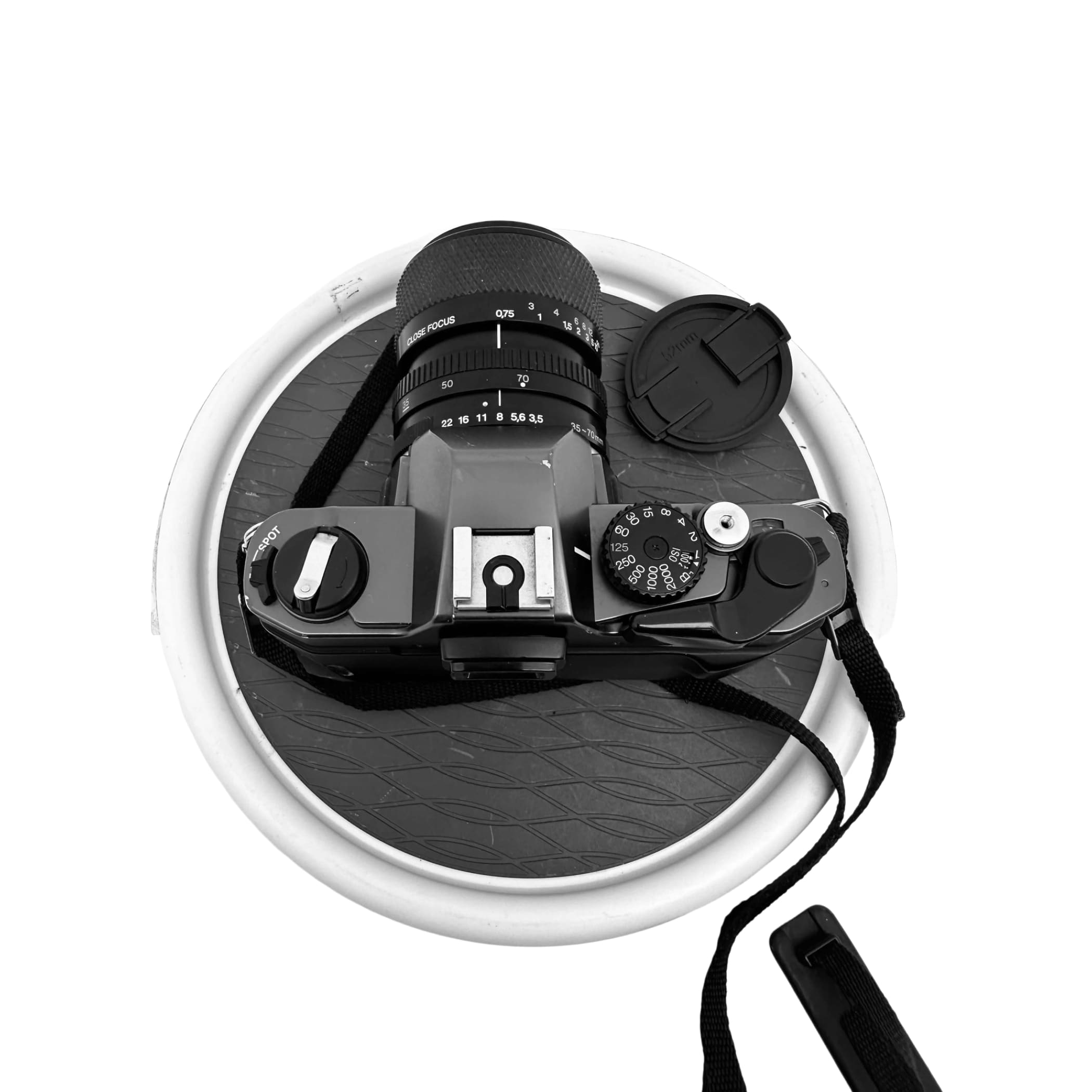 Black dslr camera with a lens cap and strap, resting on a textured circular mat.