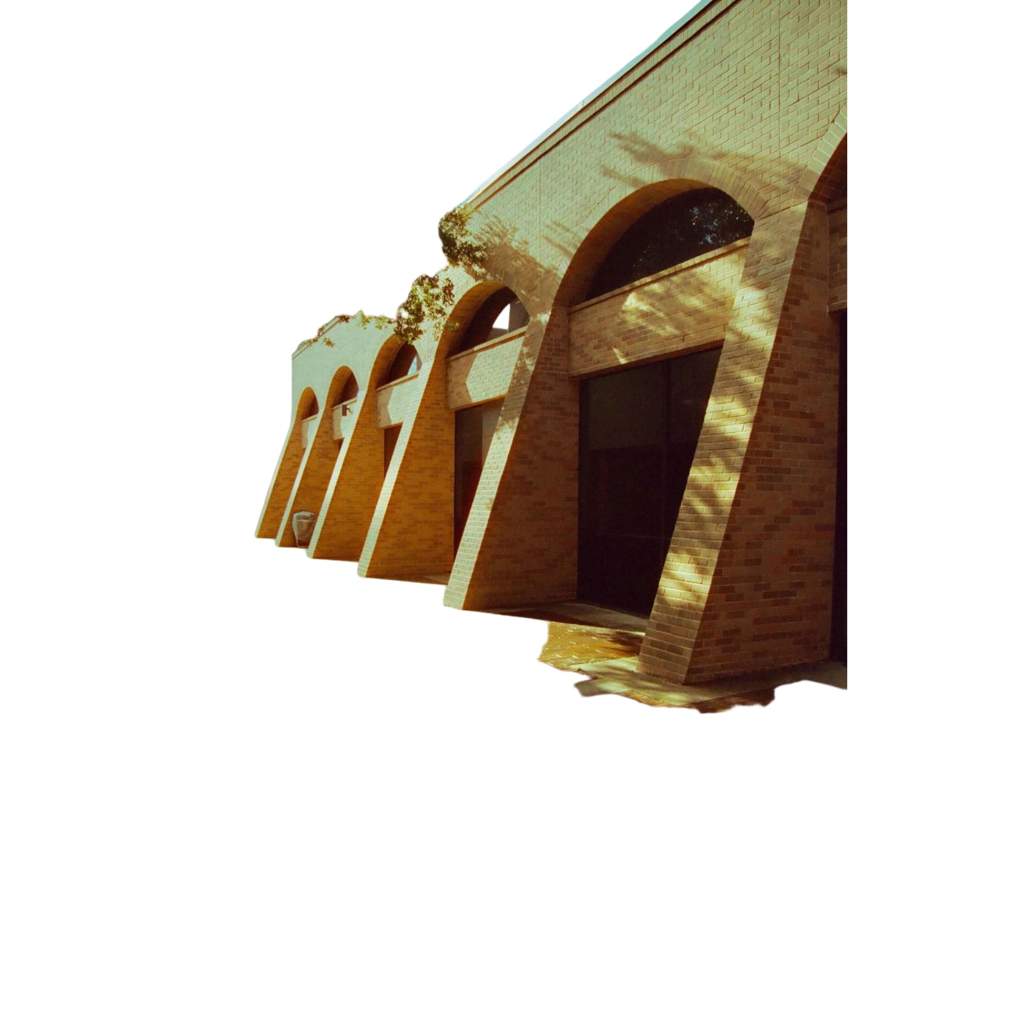 The building features a series of warm-toned brick arches with dark glass doors, set against a backdrop of trees and blue sky.