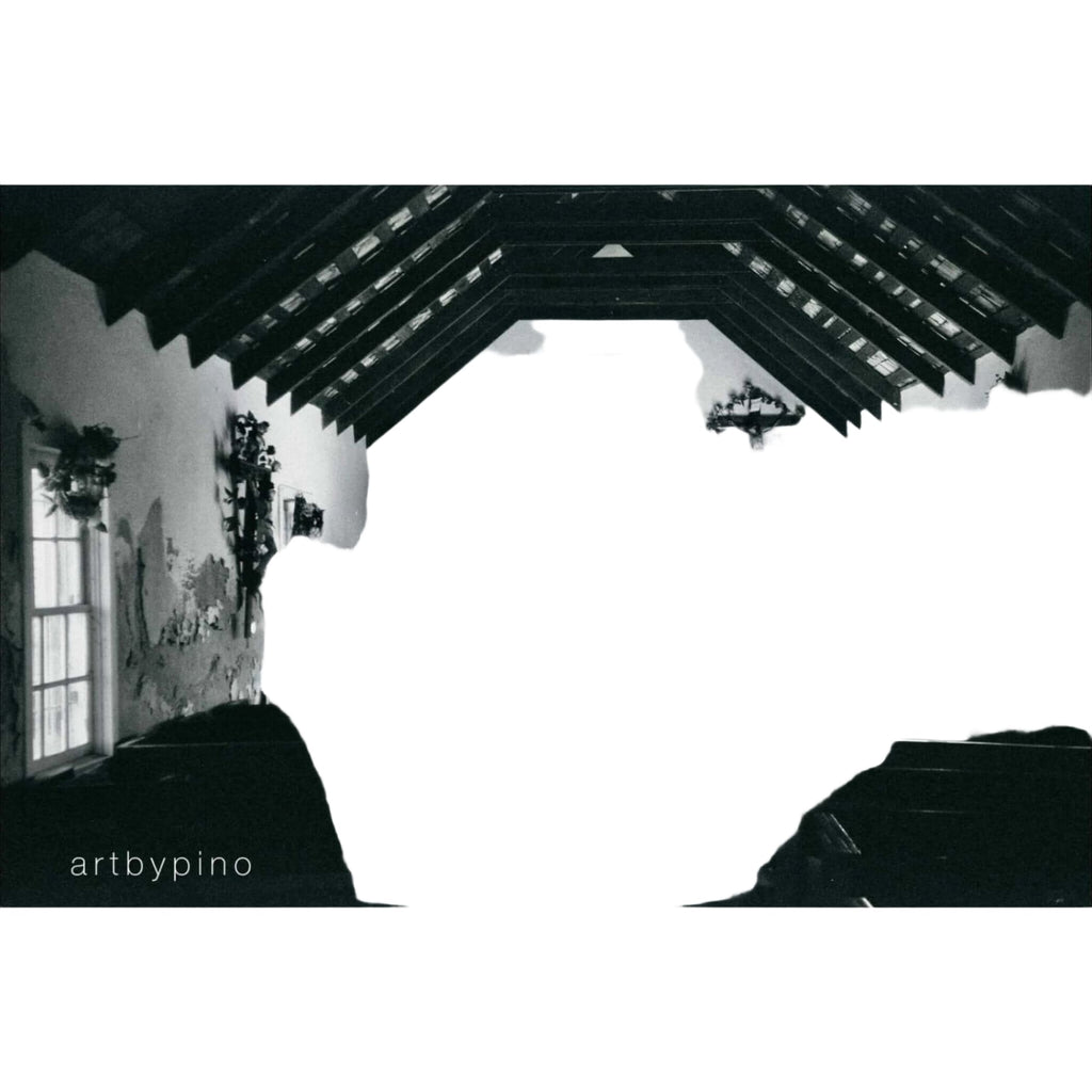 A black-and-white photograph of a rustic church interior with exposed wooden beams, floral arrangements on the altar, and pews lining the nave.