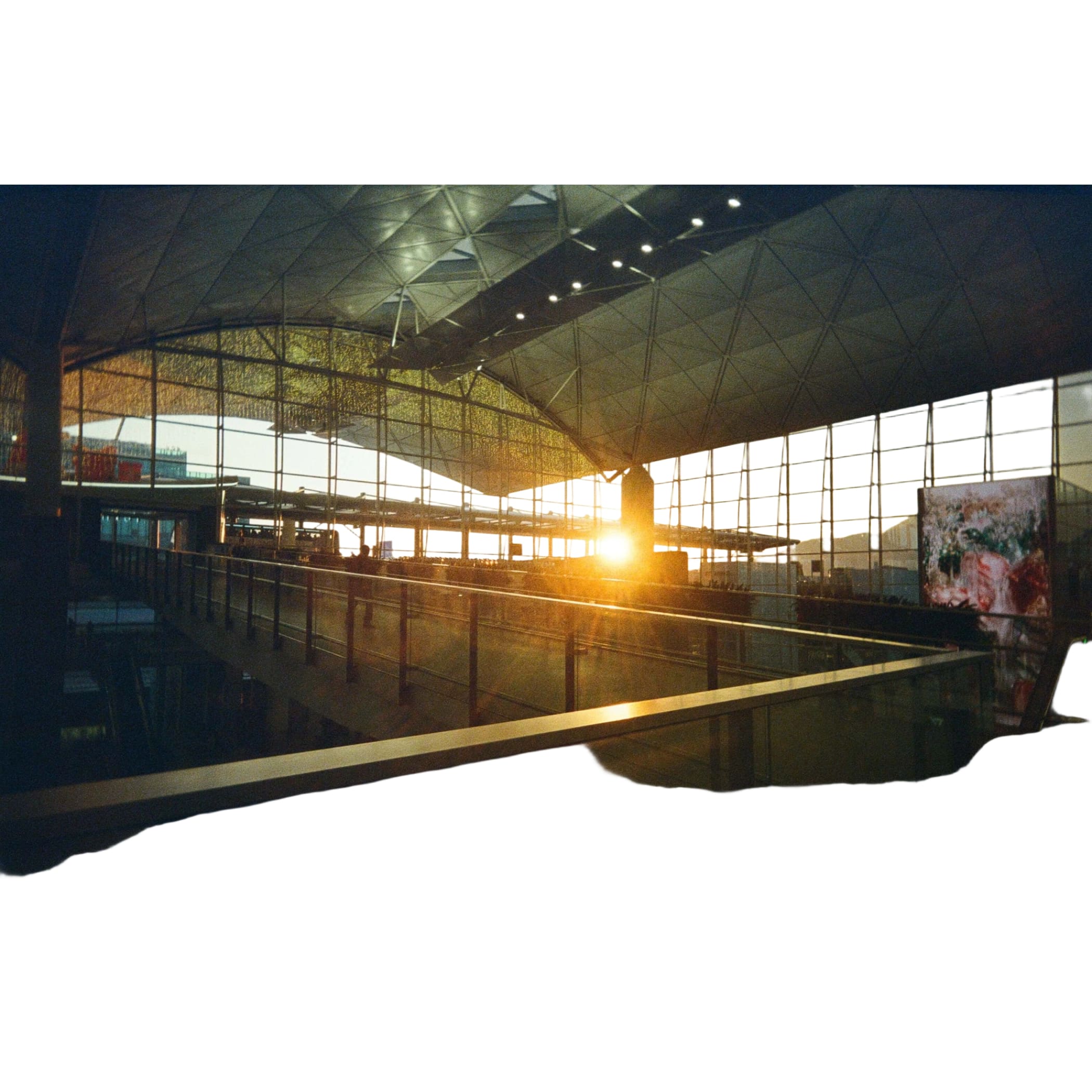 The sun sets through the glass windows of a modern, geometrically structured airport terminal.