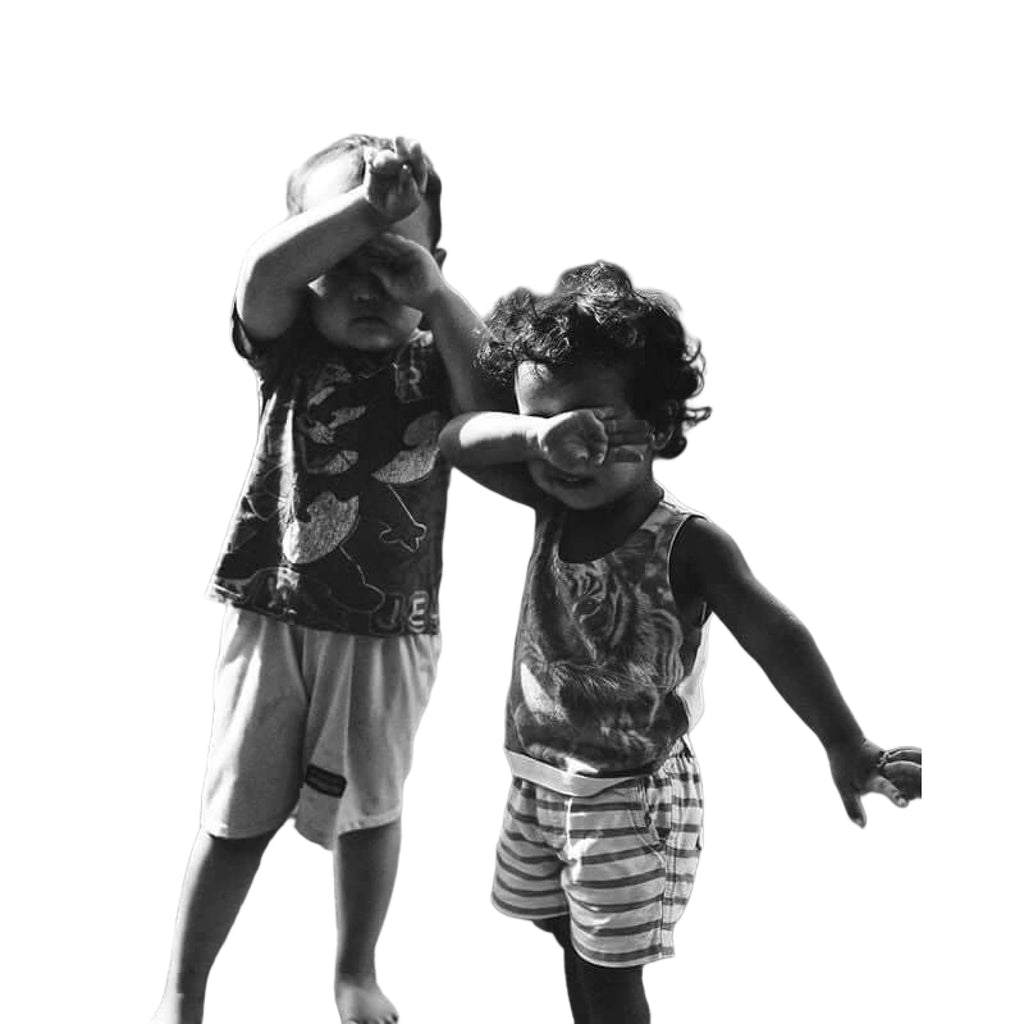Two toddlers, one in a patterned short-sleeved shirt and light shorts, the other in a sleeveless top with tiger print and striped shorts.