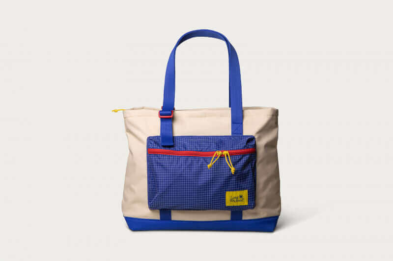 Beige and blue tote bag with front zippered pocket and blue handles on a white background.