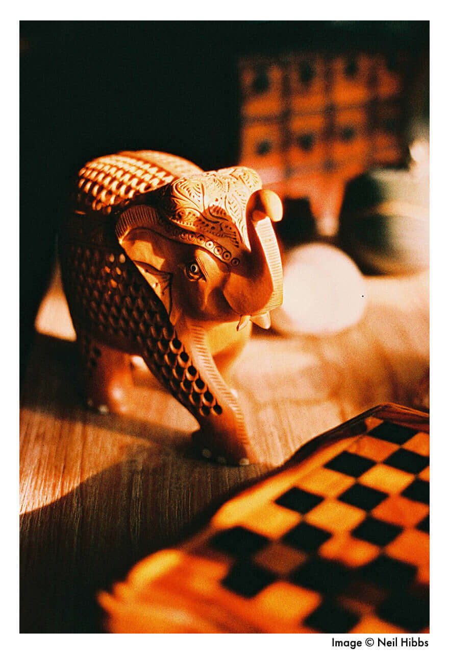 Intricately carved wooden elephant sculpture on display with a checkered board pattern in the foreground.