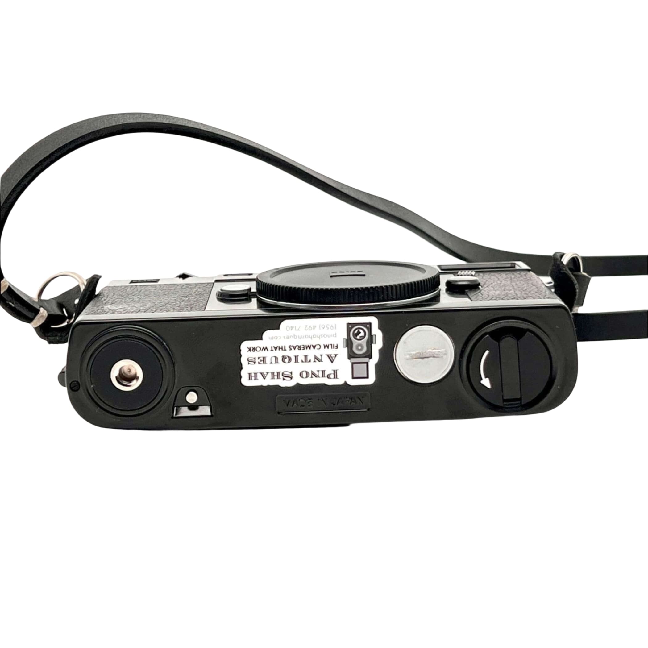 Black textured body with a silver shutter button and black leather strap, featuring a sticker that reads ’pino shah antiques film cameras that work.’