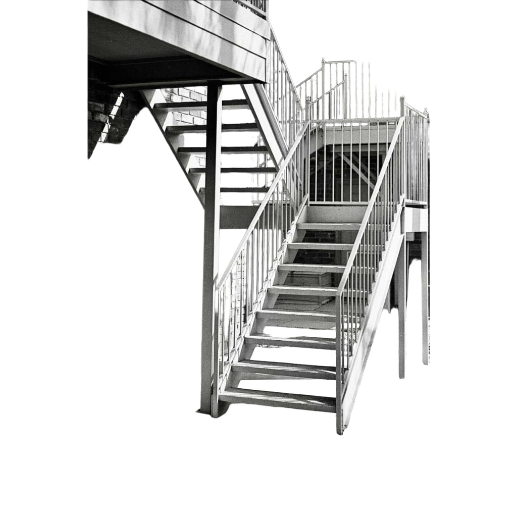Metallic staircase with vertical railings and concrete steps against a brick wall