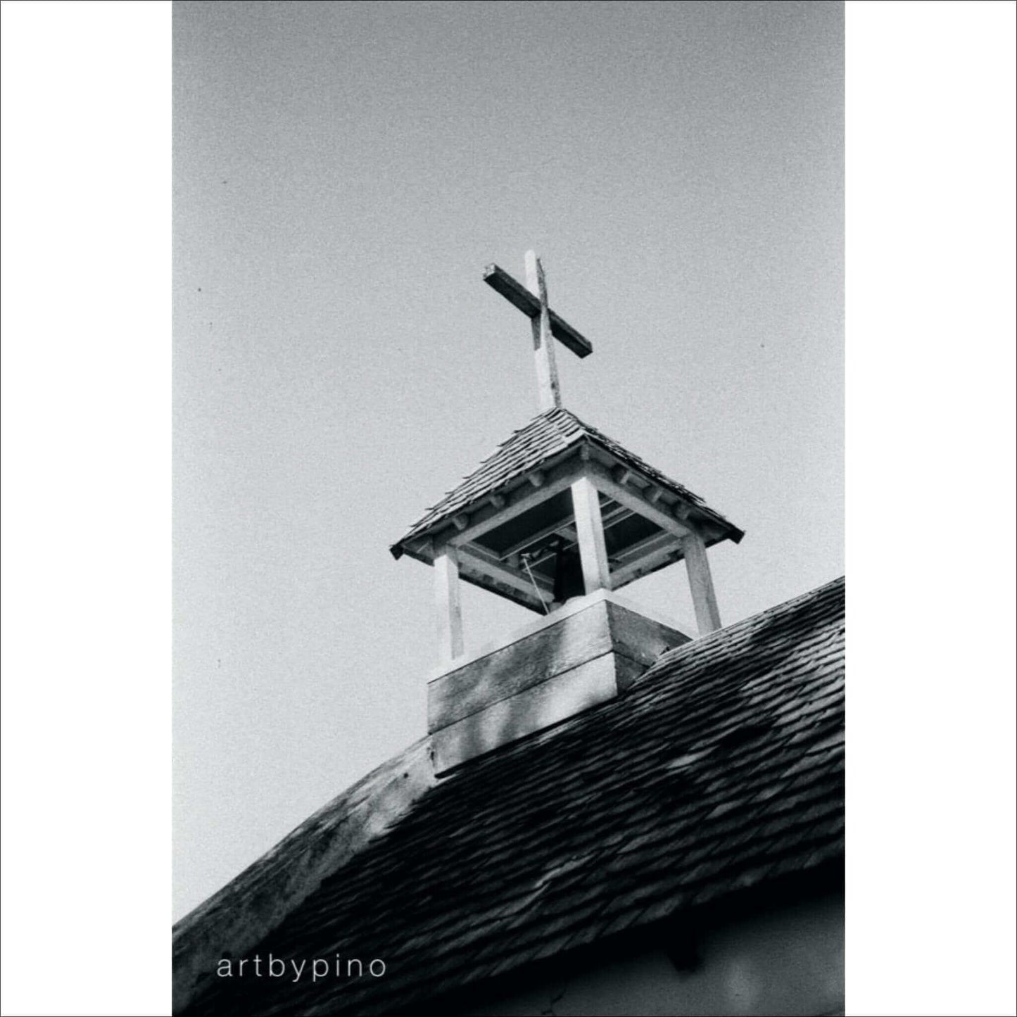 Black and white image of a church steeple with a cross against a gray sky.