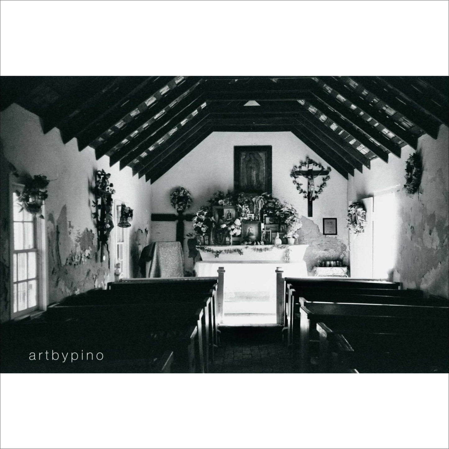 Interior of a quaint church with wooden benches and an altar, captured in black and white photography.
