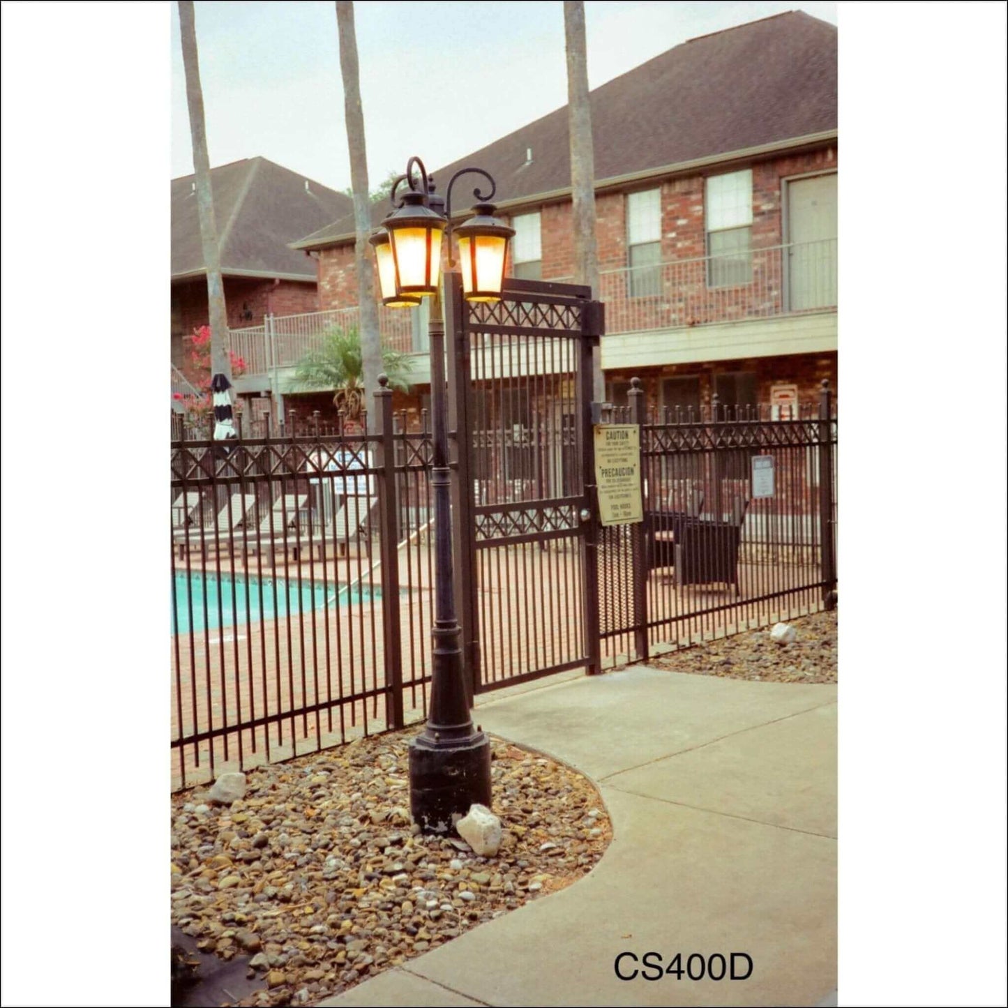 Vintage street lamp illuminating a gated pool area with brick buildings in the background.