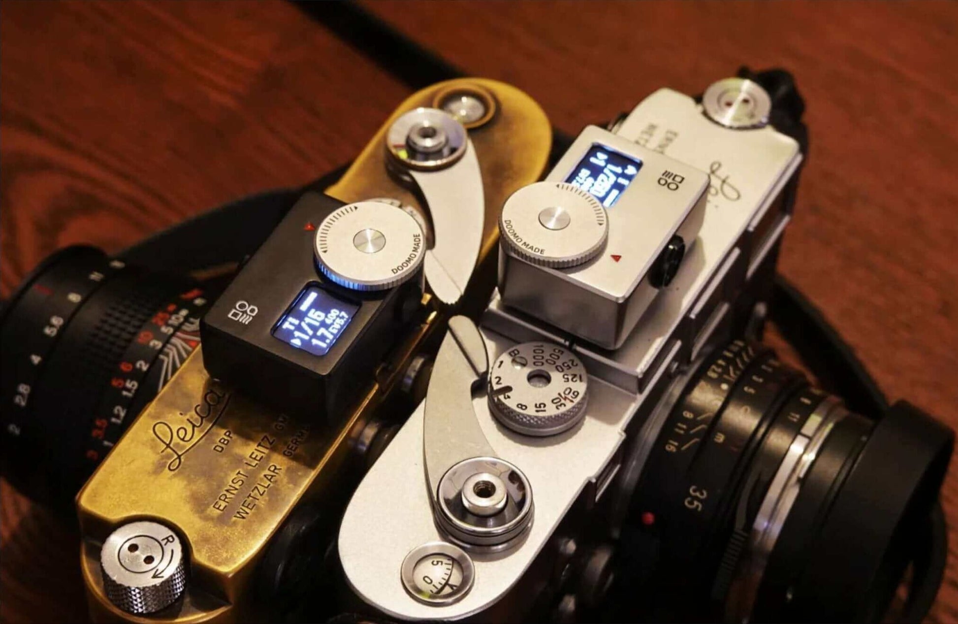 Two vintage Leica cameras with digital light meters on a wooden table.