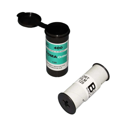 Two 120mm film canisters, one upright with a black lid and green label, and one lying down with a white label, on a teal surface.