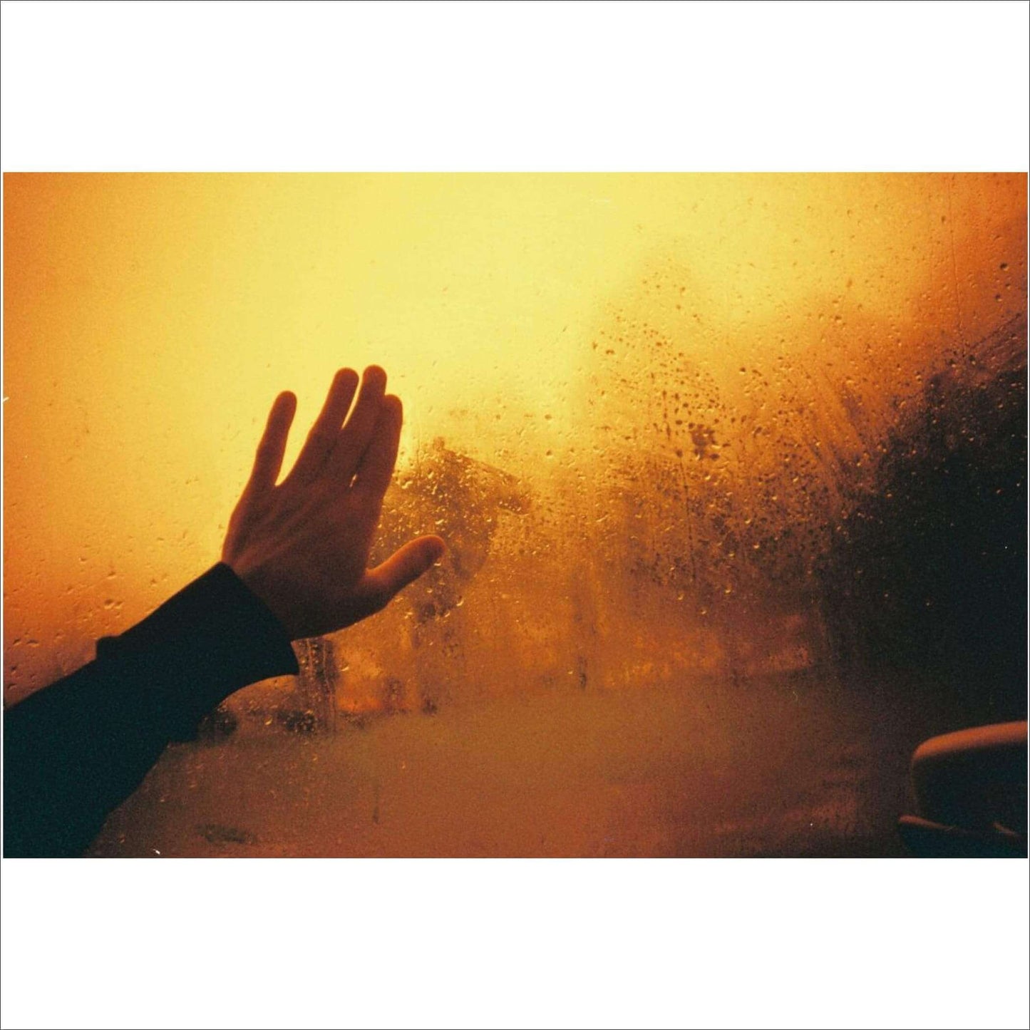 Hand pressed against a foggy window with an orange hue, capturing a moment of warmth and introspection.