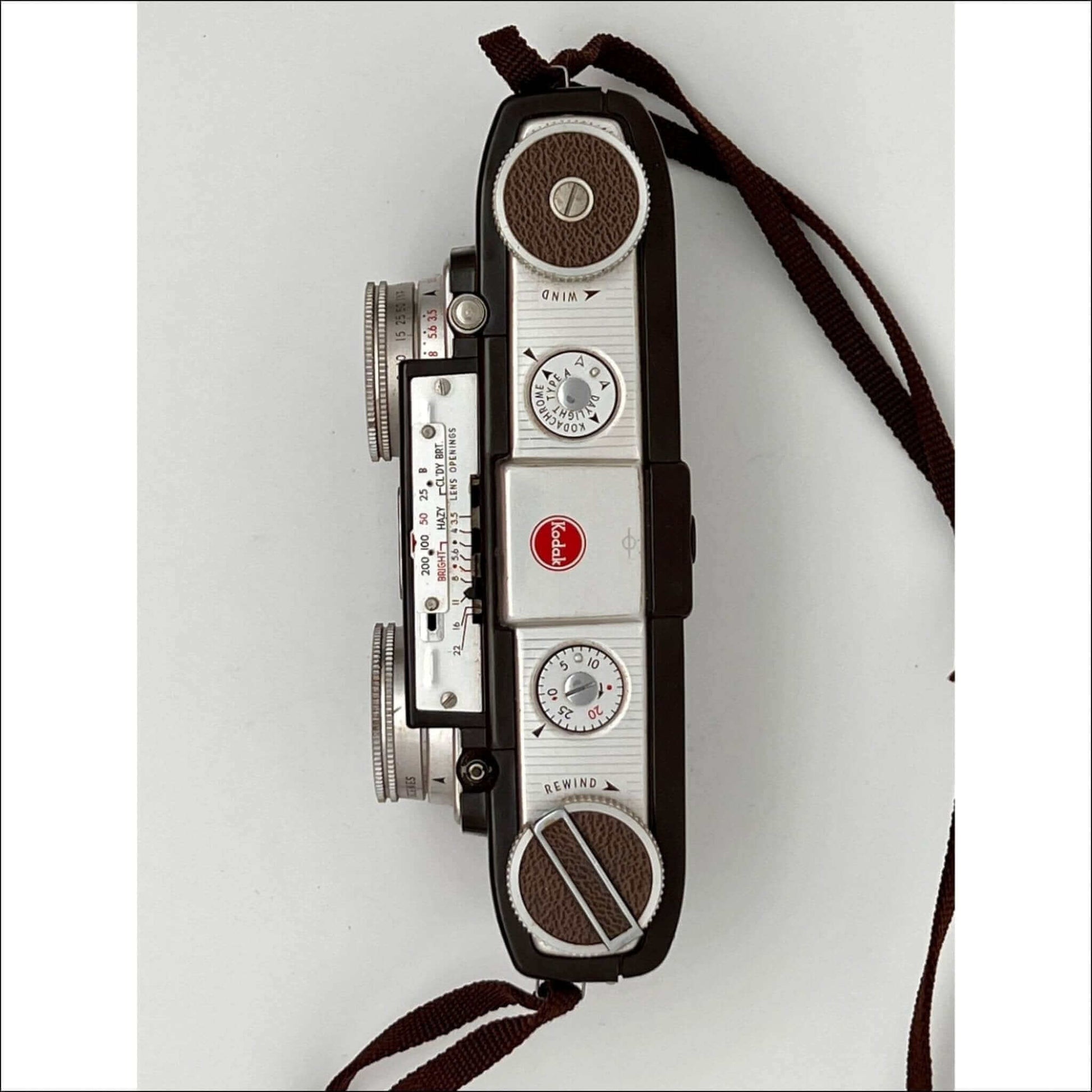 Top view of a vintage camera with dials, leather accents, and a red logo, equipped with a brown strap.