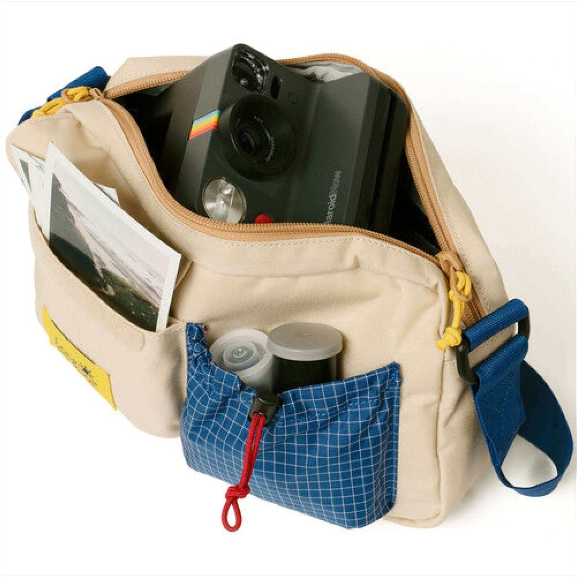 Open beige and blue camera bag with a Polaroid camera, film cannisters, and photographs inside.