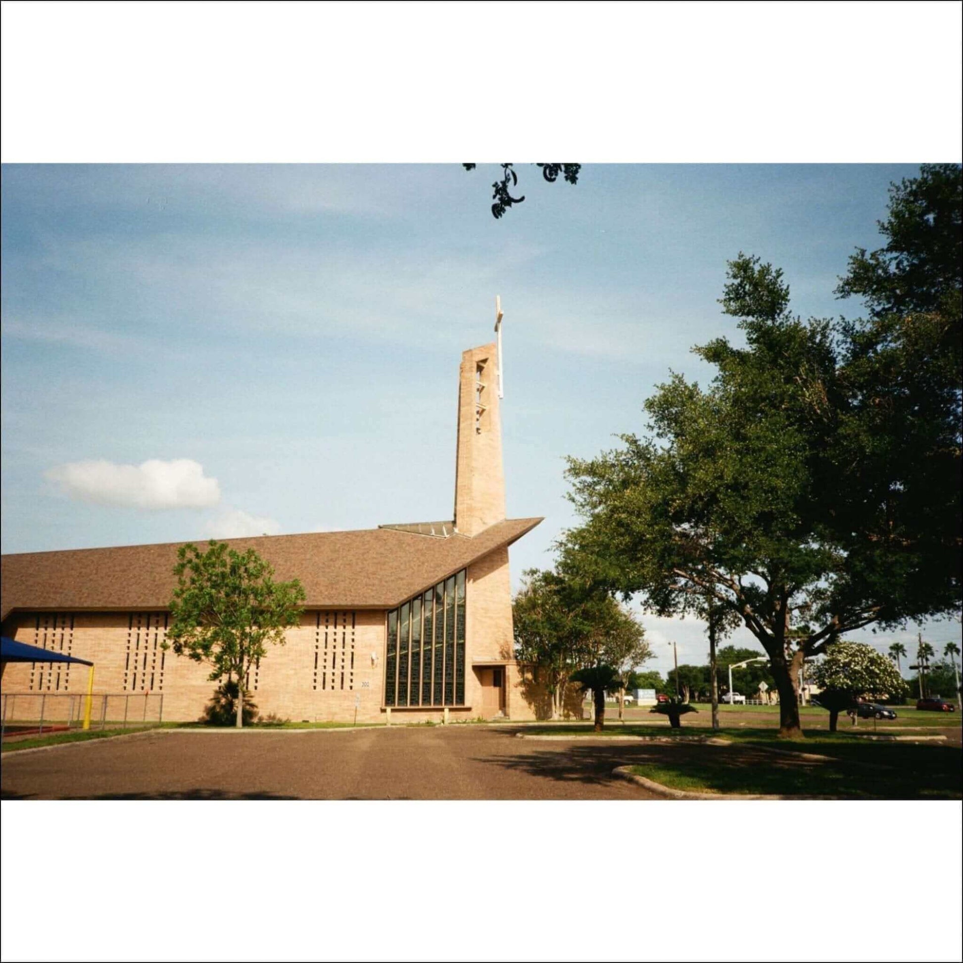 Side view of a modern church with a tall tower, surrounded by trees and a grassy area.
